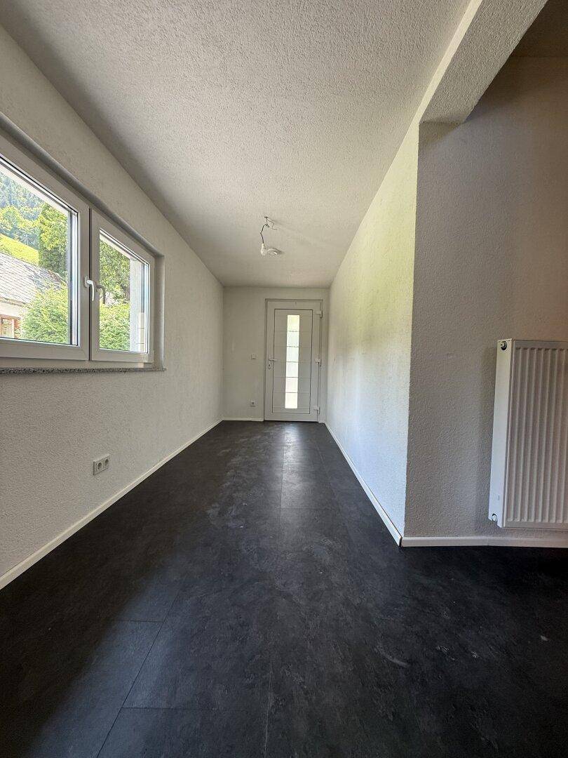 Heller Eingangsbereich mit dunklem Boden, Fenstern und einer modernen Haustür.