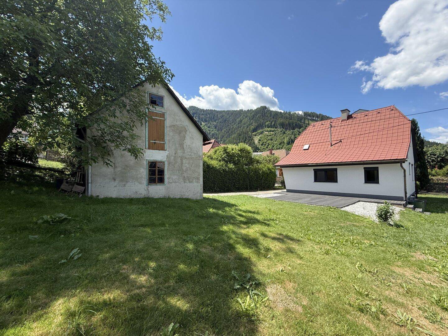 Großer Gartenbereich mit Rasenfläche, altem Nebengebäude und dem Haupthaus im Hintergrund.