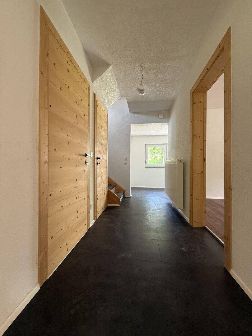 Heller Flur mit dunklem Boden, Holztüren und Blick in einen weiteren Raum.