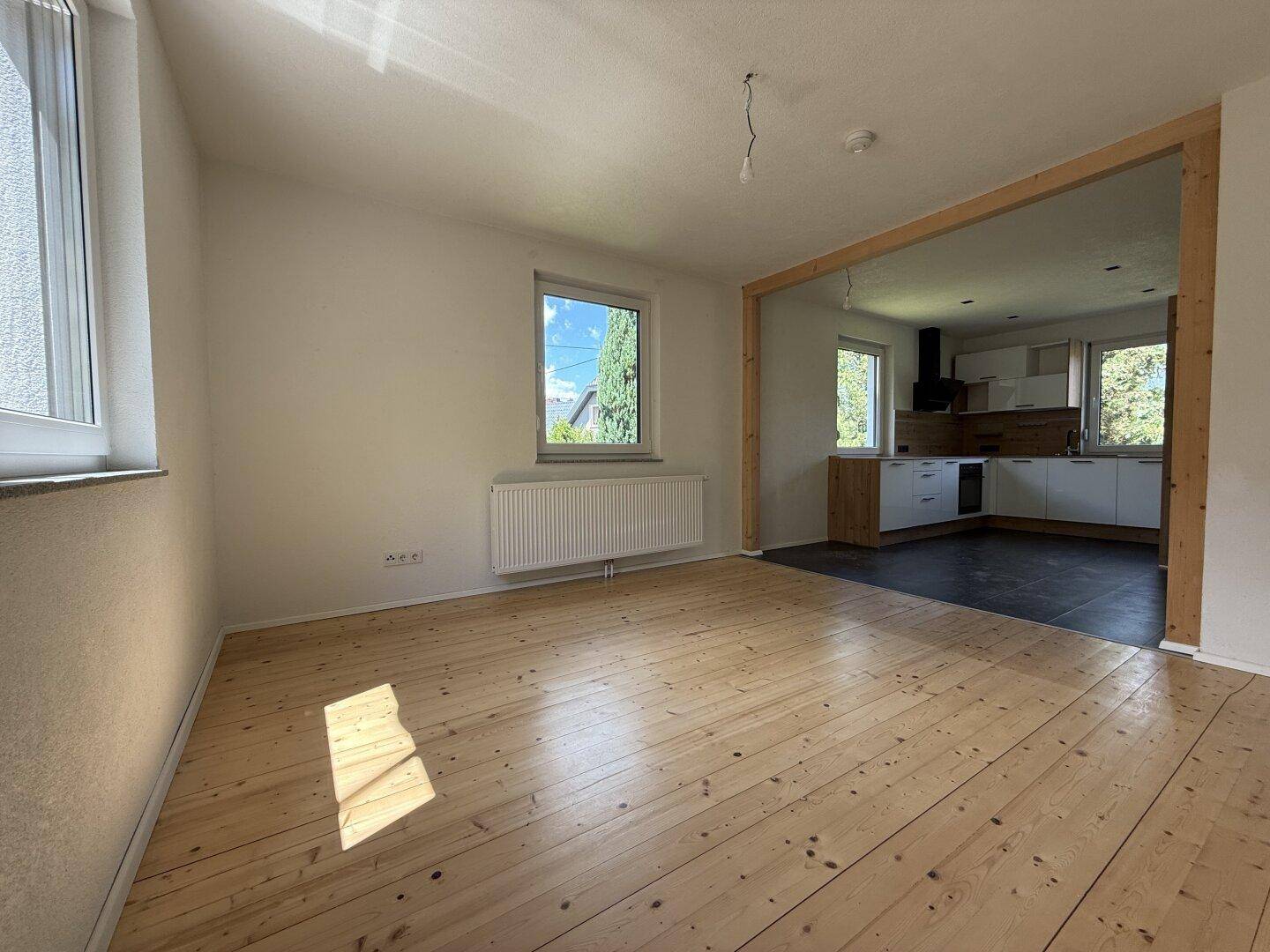 Helles Wohnzimmer mit Holzdielenboden und Blick in die moderne Küche.