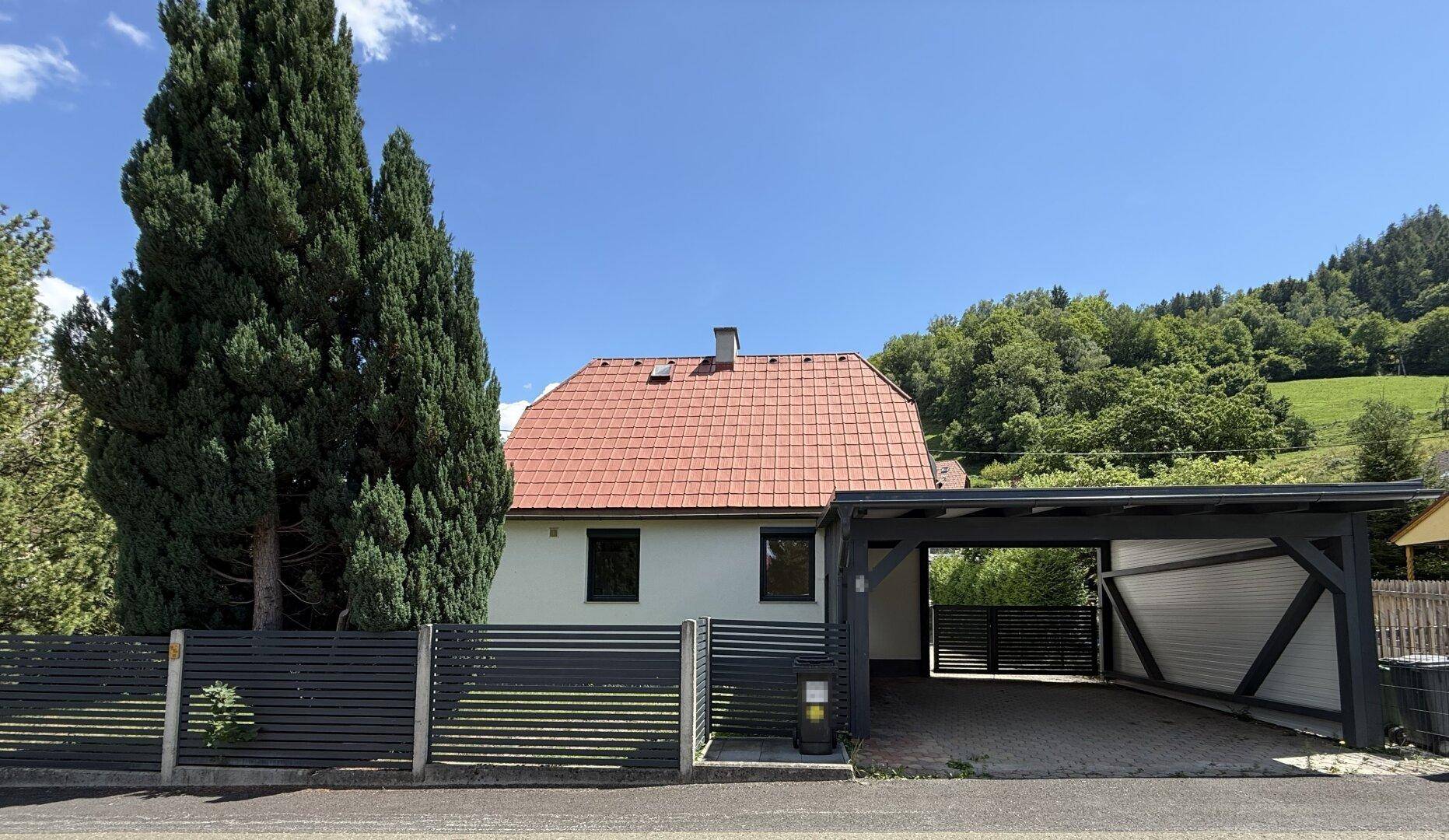 Vorderansicht des Hauses mit Carport und gepflegtem Vorgarten unter blauem Himmel.