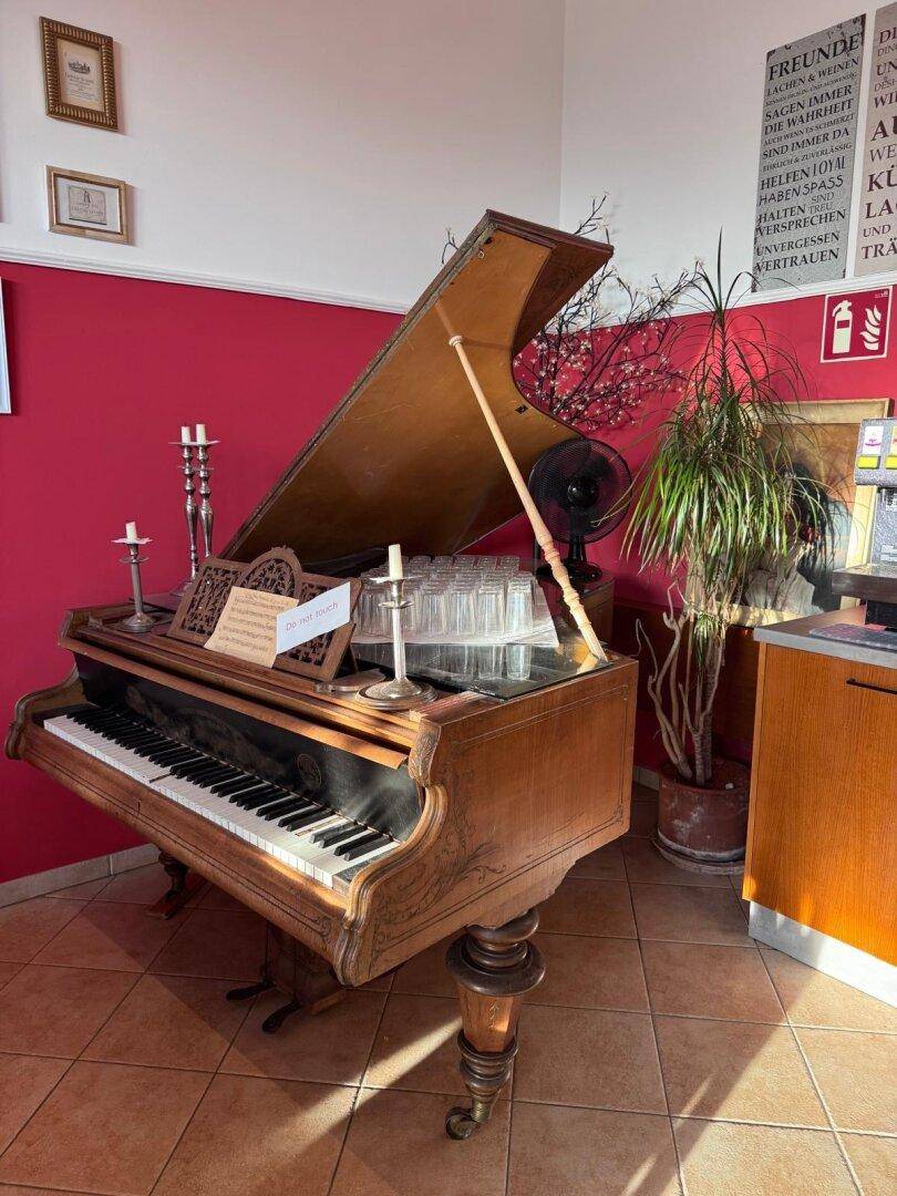 Antiker Flügel in einem Restaurantbereich mit roten Wänden und Fliesenboden, bereit für musikalische Unterhaltung.