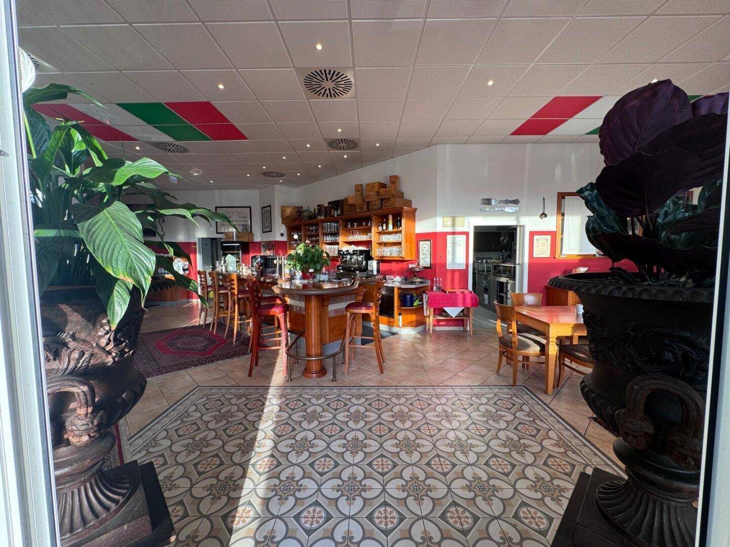 Blick auf den Barbereich eines Restaurants mit Holztresen, Barhockern und einem gemusterten Fliesenboden.
