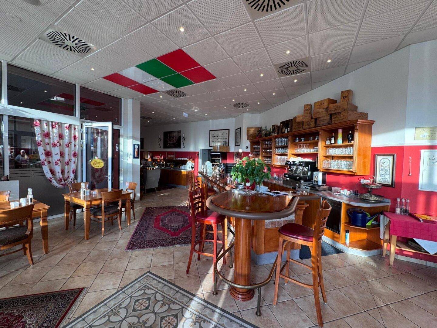 Heller Barbereich eines Restaurants mit Holztresen, Barhockern und mehreren Tischen, die zum Verweilen einladen.