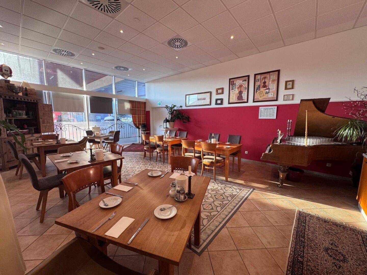 Restaurantbereich mit Holztischen, Fliesenboden und einem antiken Holzschrank neben der roten Akzentwand.