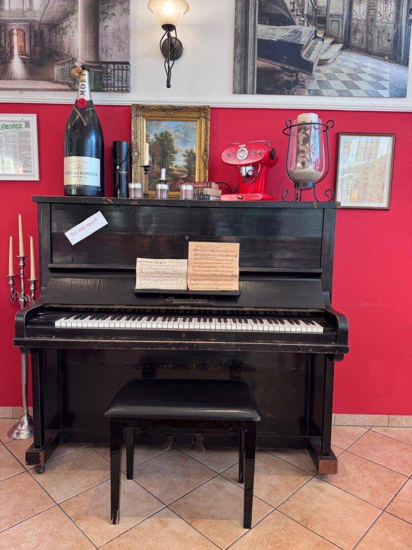 Schwarzes Klavier an einer leuchtend roten Wand, umgeben von dekorativen Elementen und einem großen Champagnerflasche.
