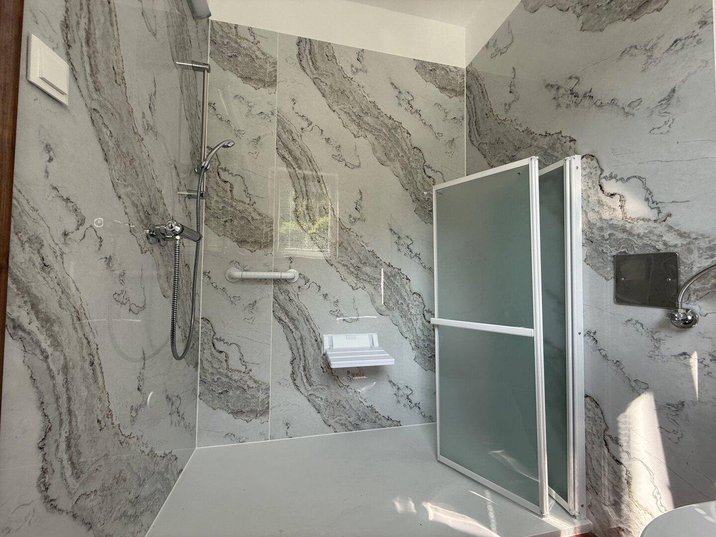 Modernes Badezimmer mit großformatigen Fliesen, barrierefreier Dusche und Haltegriffen.