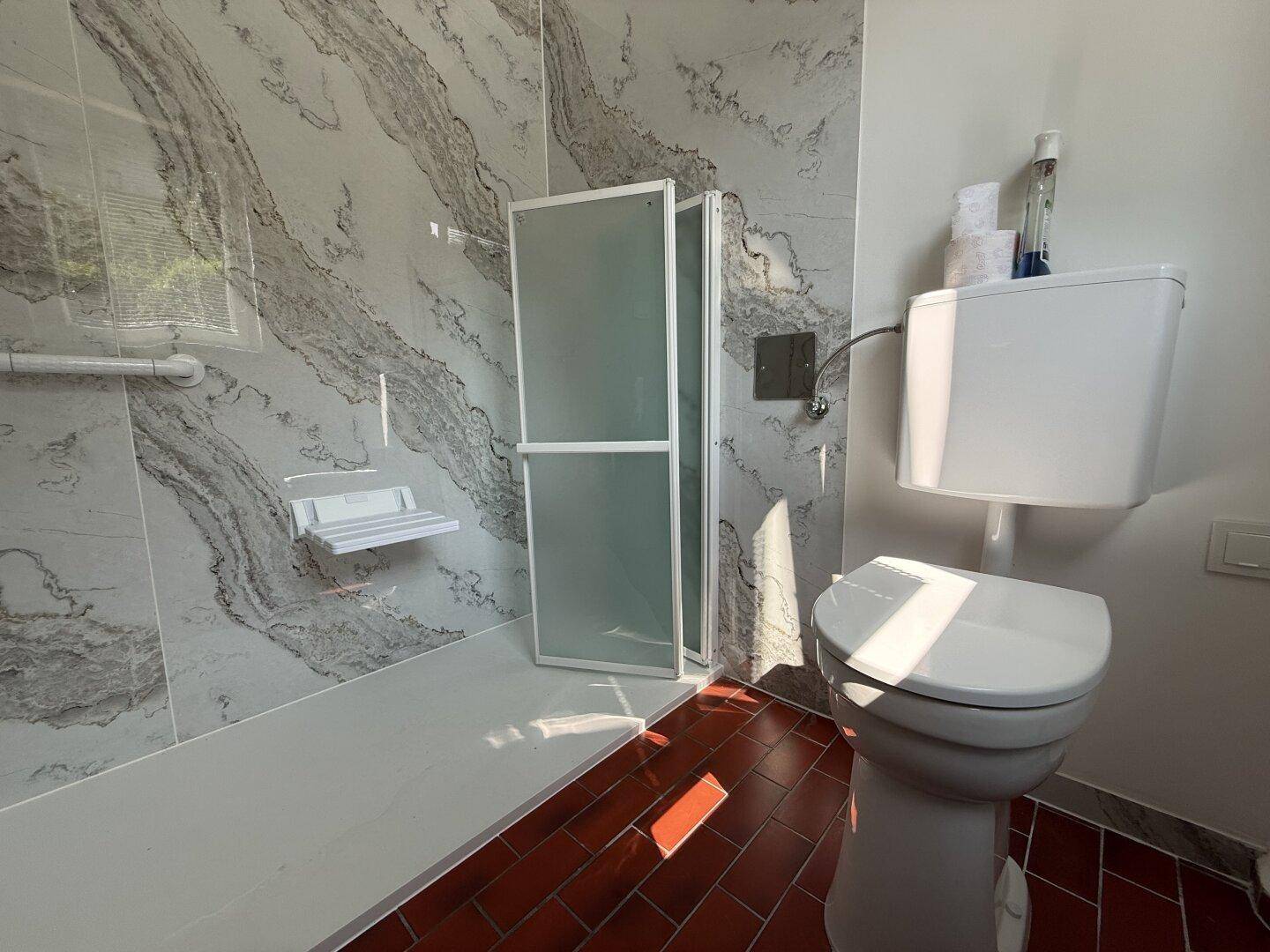 Badezimmer mit WC, barrierefreier Dusche und einer Kombination aus modernen und traditionellen Fliesen.