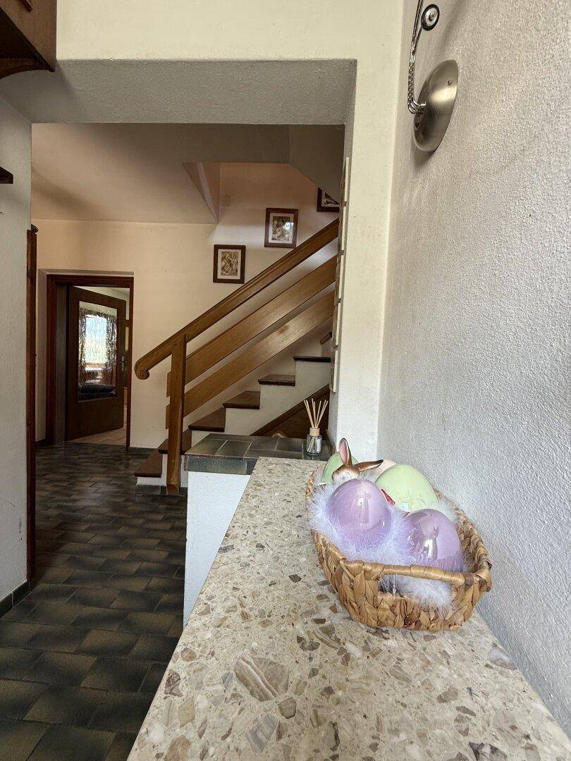 Eingangsbereich mit gefliestem Boden, Holztreppe und einer Konsole mit Dekoration.