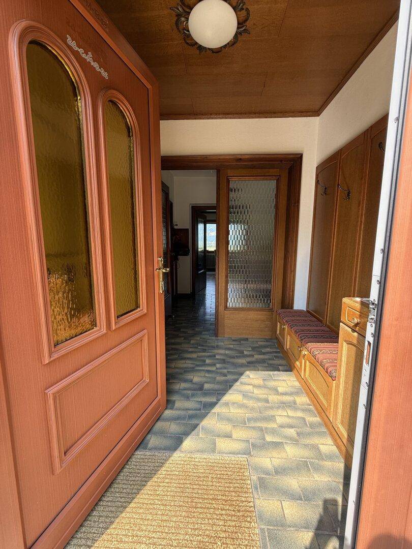 Heller Eingangsbereich mit Holztür, gefliestem Boden und integrierter Garderobe.