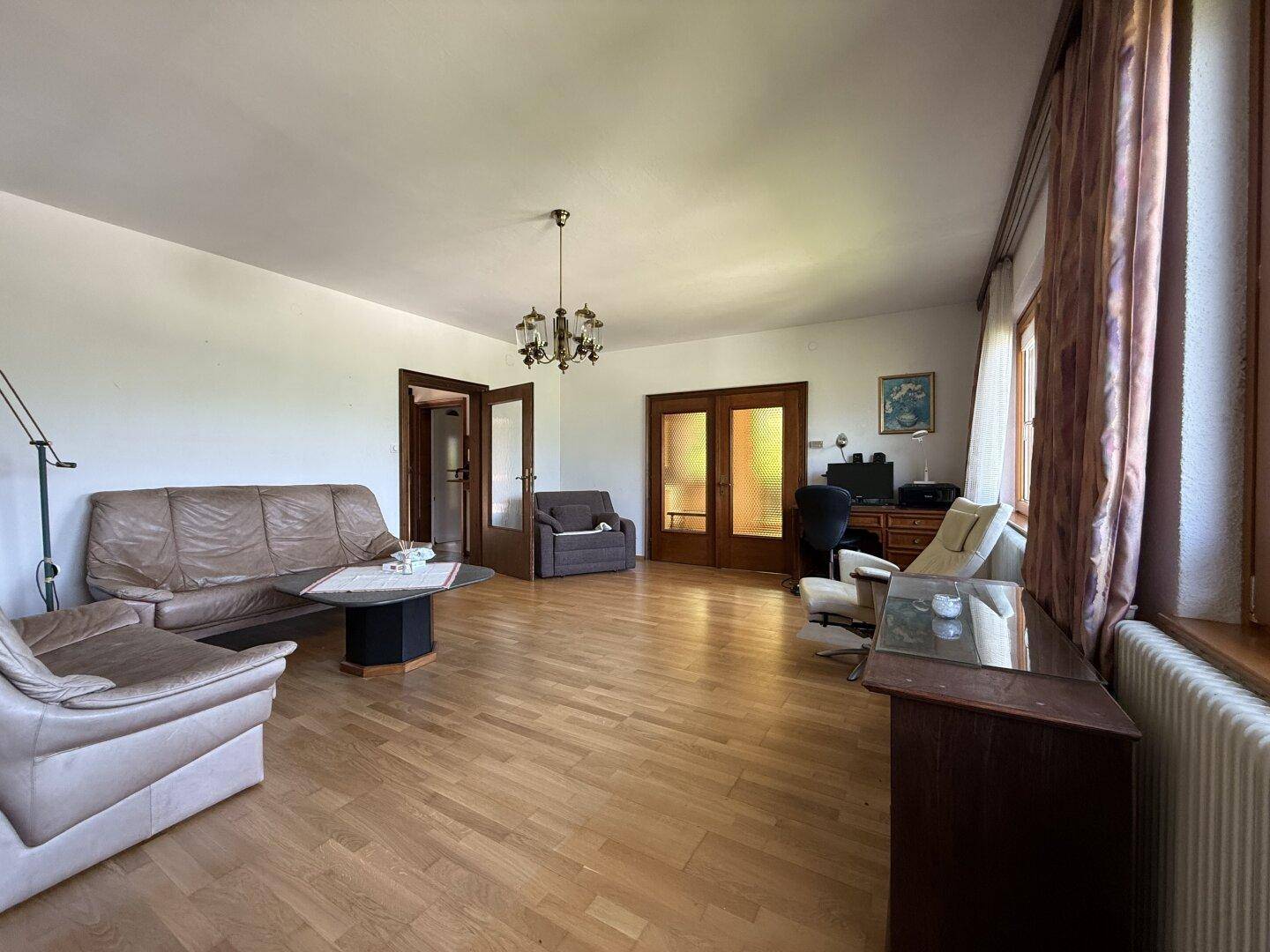 Helles Wohnzimmer mit Parkettboden, gemütlichen Sitzgelegenheiten und Zugang zu weiteren Räumen.