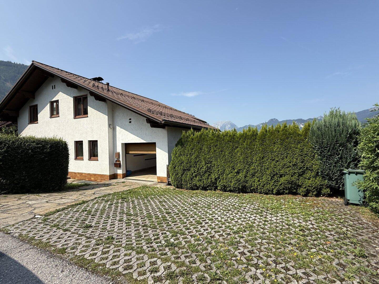 Ansicht des Hauses mit gepflasterter Einfahrt, grünen Hecken und Satteldach.