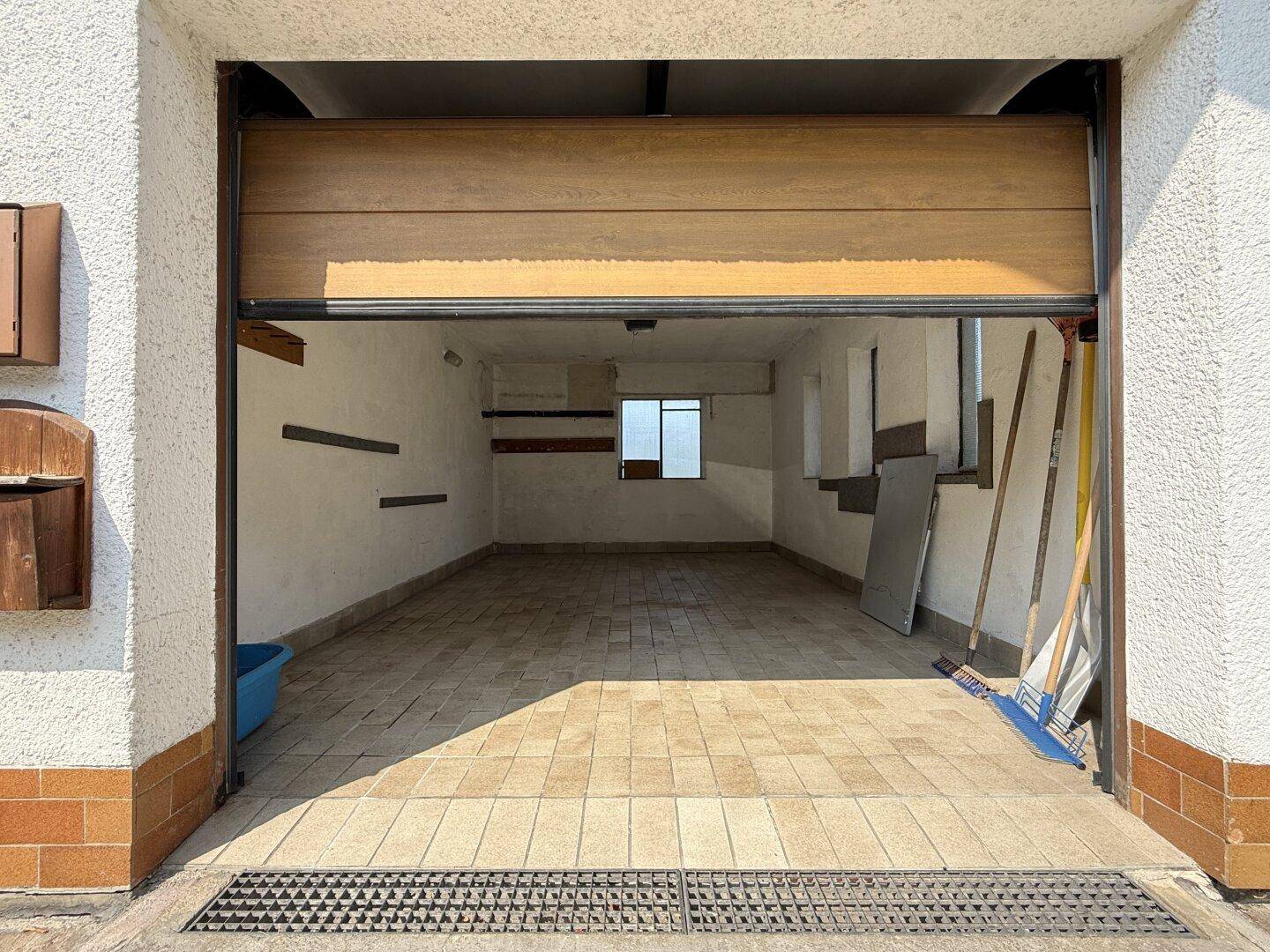 Leere Garage mit gefliestem Boden und offenem Garagentor, bereit zur Nutzung.