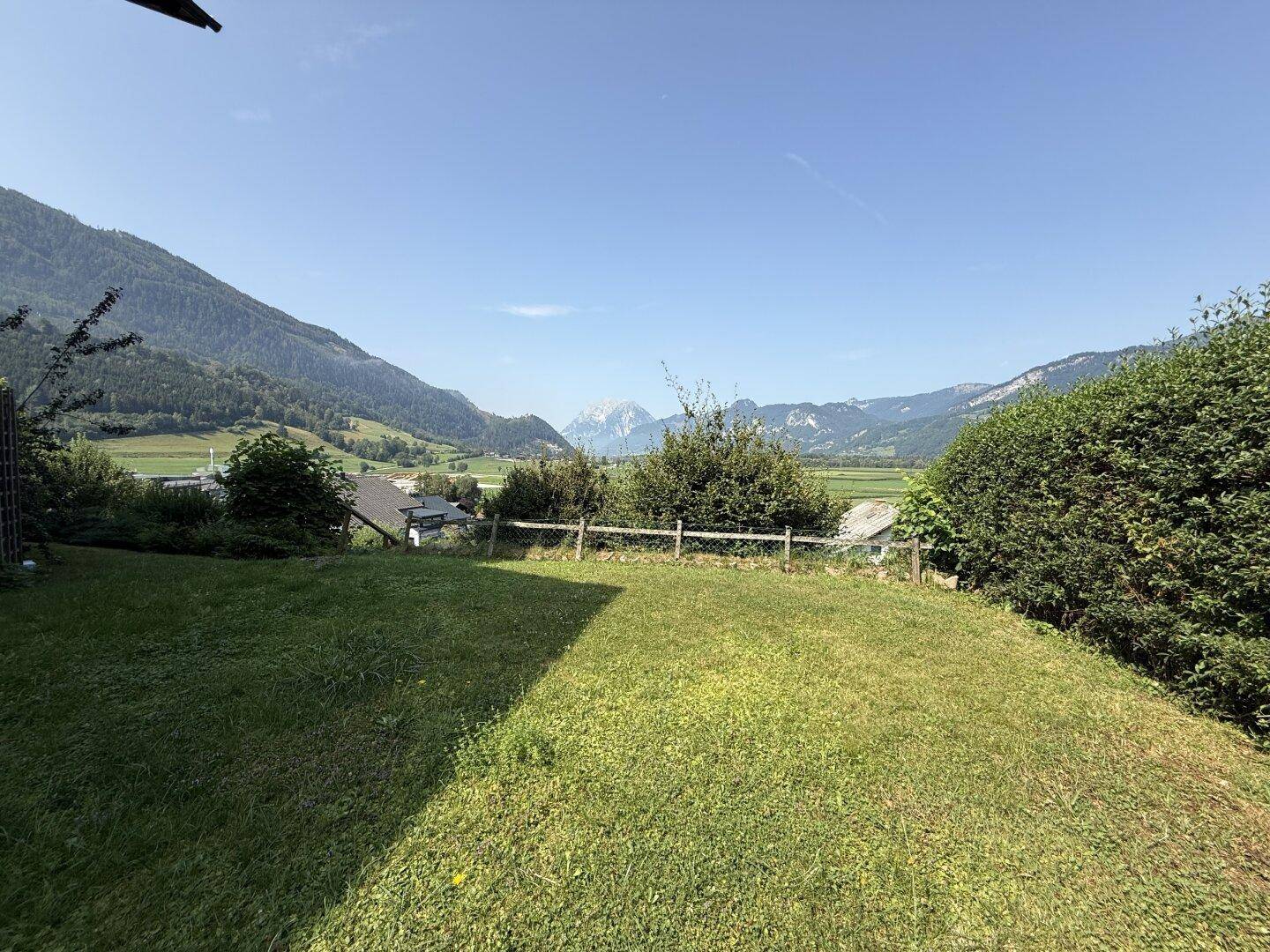 Gepflegter Rasenbereich mit Hecke und Zaun, der einen weiten Blick auf die Berge bietet.