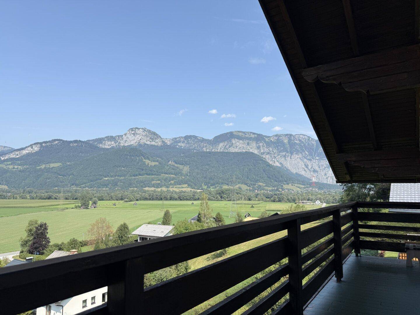 Blick vom traditionellen Holzbalkon auf die weite grüne Landschaft und die umliegenden Berge.