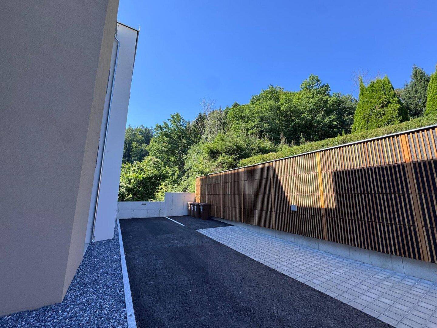 Außenbereich mit Parkplätzen und einer modernen Holzverkleidung als Sichtschutz.