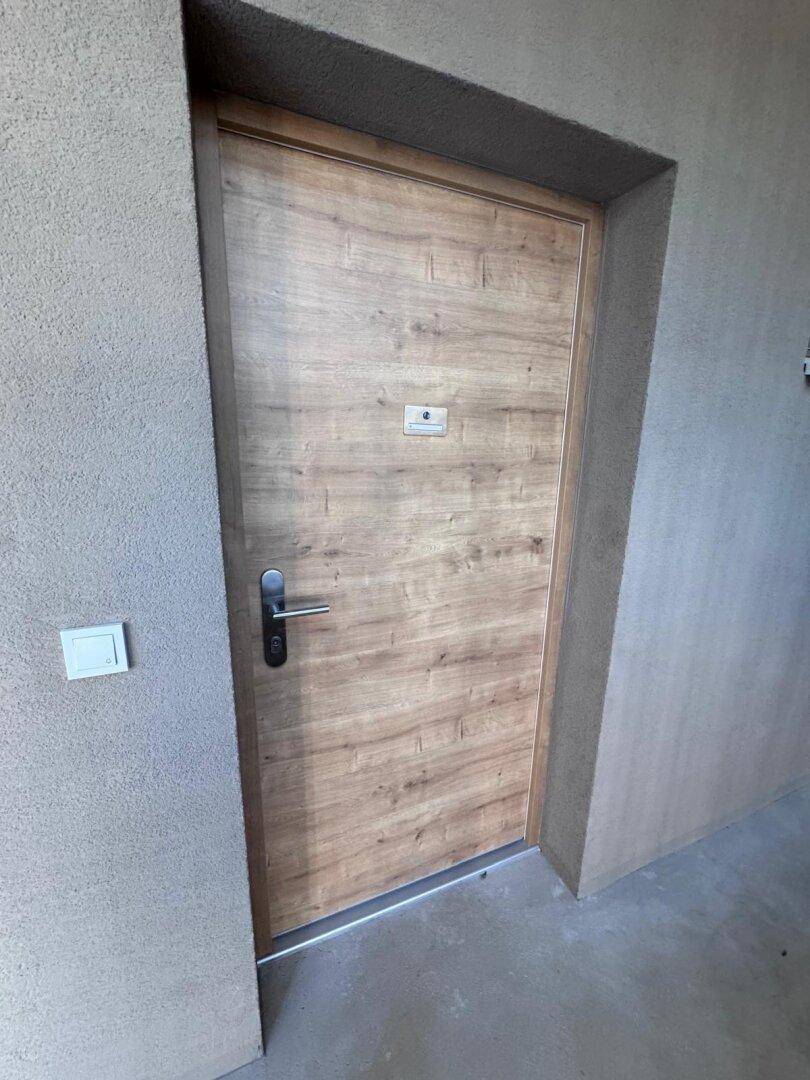 Moderne Wohnungseingangstür aus Holz in einem Flur mit grauen Wänden.