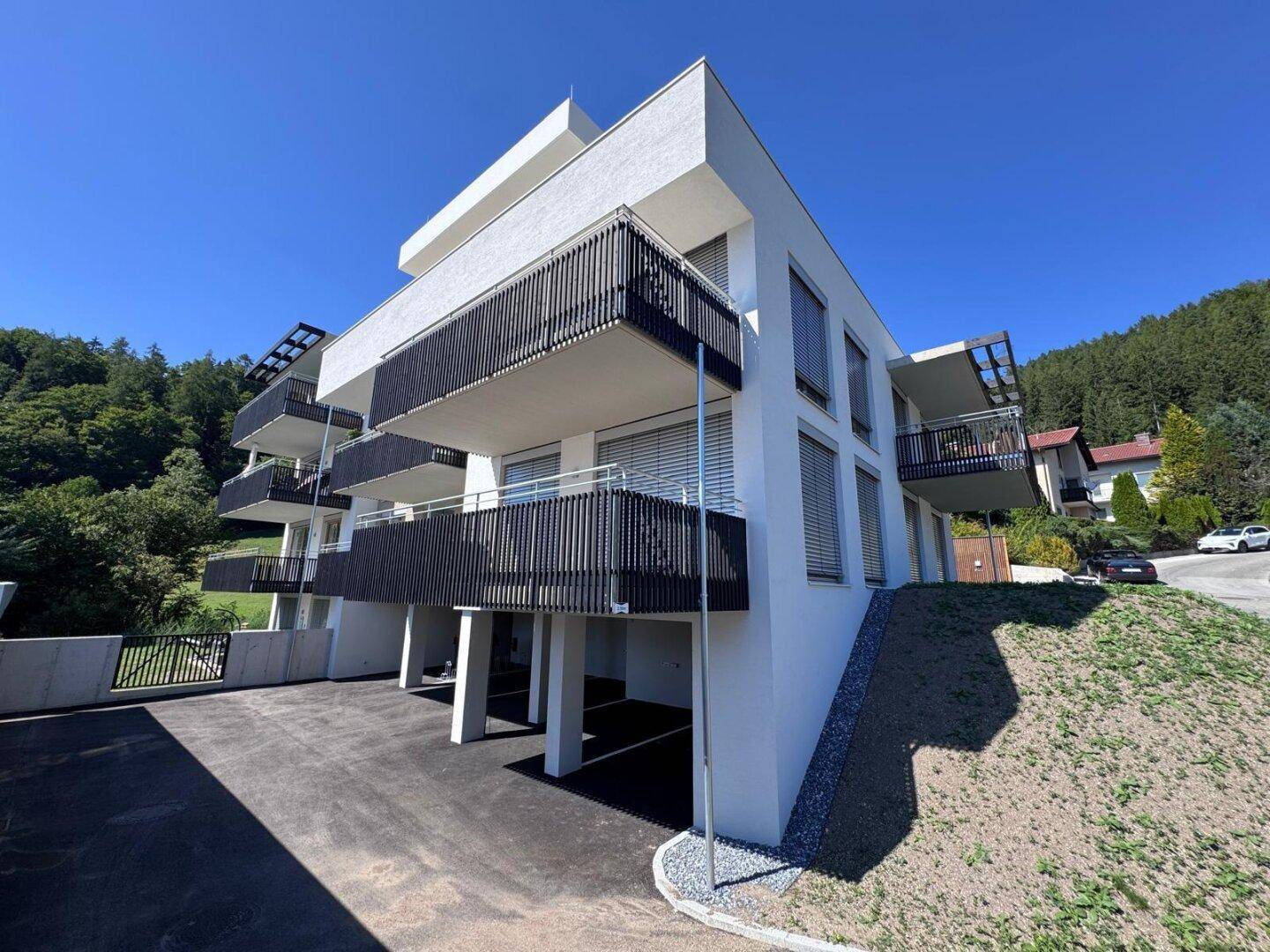 Ansicht eines modernen Mehrfamilienhauses mit mehreren Balkonen und Parkplätzen im Freien.