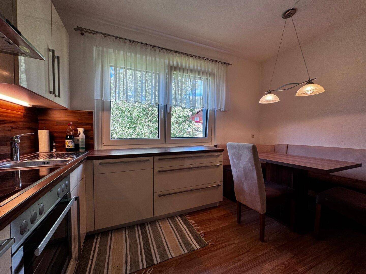 Gemütlicher Essbereich in der Küche mit Eckbank, Holztisch und Blick ins Grüne durch das Fenster.