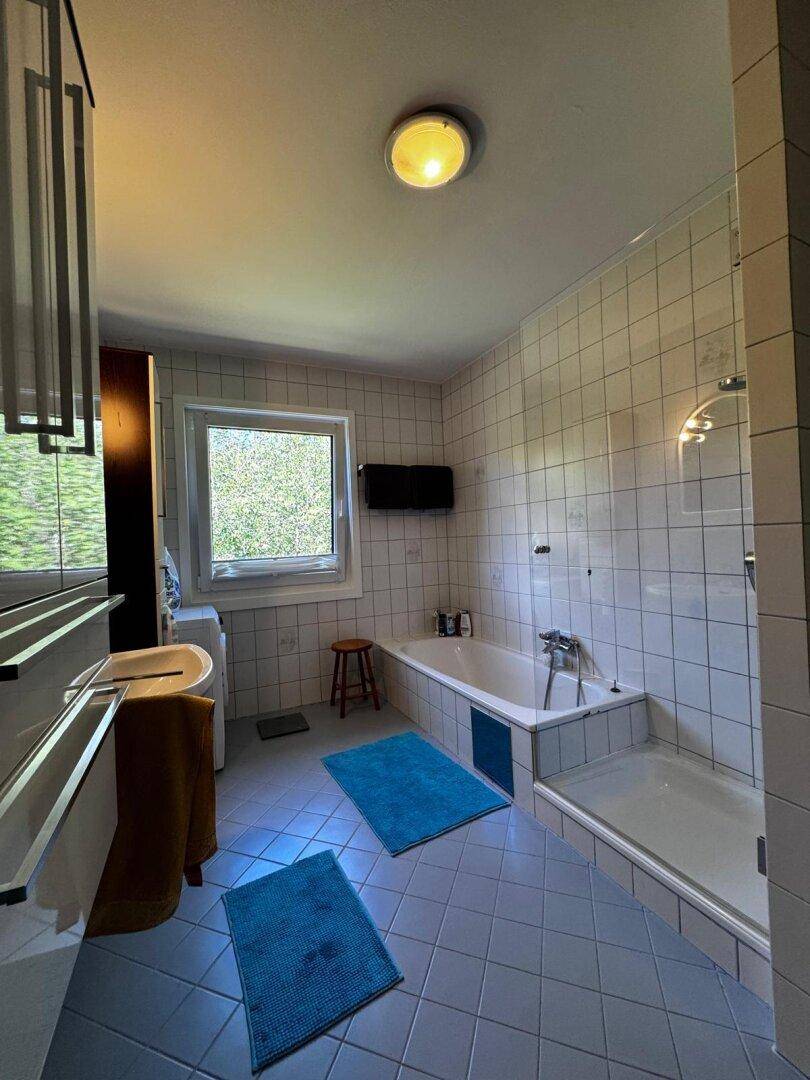 Helles Badezimmer mit weißen Fliesen, Badewanne, separater Dusche und Fenster für Tageslicht.