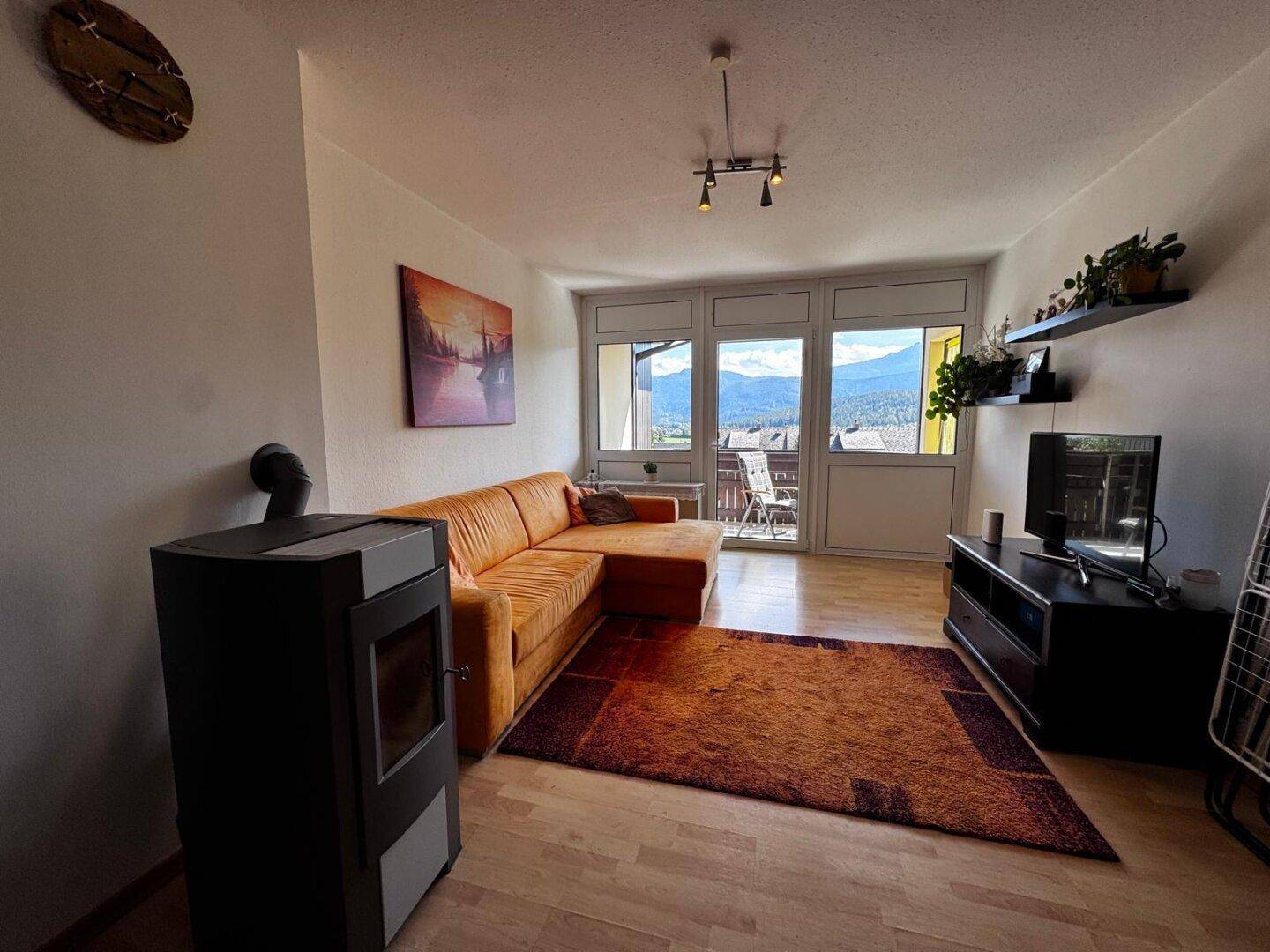 Geräumiges Wohnzimmer mit bequemer Couch, Fernseher und großen Fenstern mit Panoramablick.