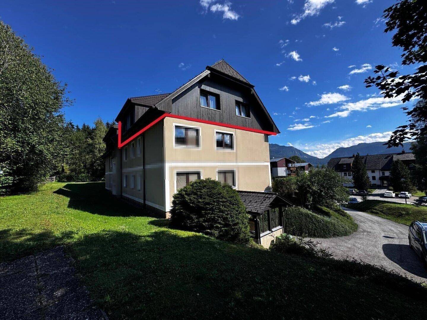 Seitenansicht des Gebäudes mit moderner Architektur, umgeben von viel Grün und Bergen im Hintergrund.