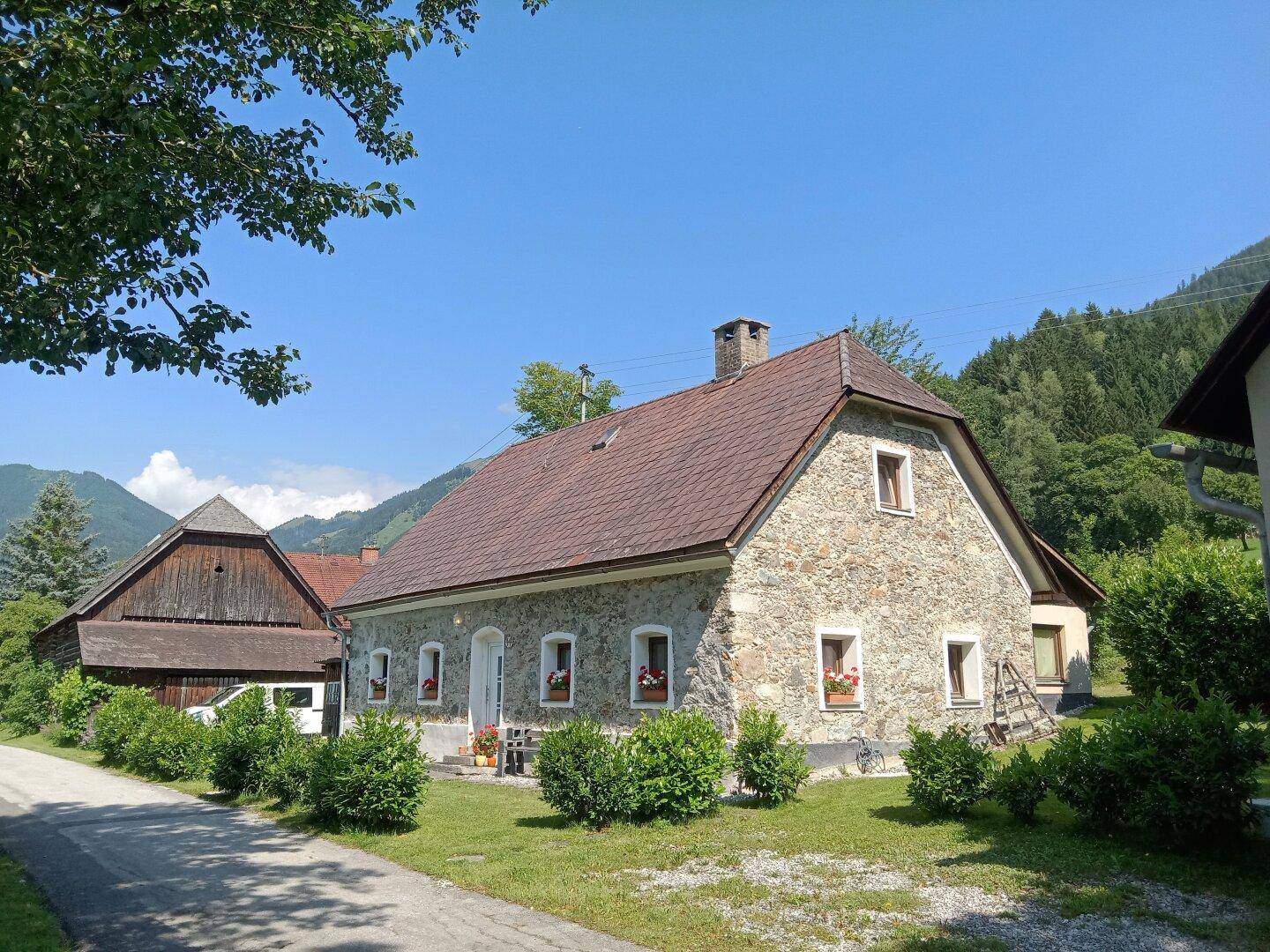 Charmantes Steinhaus mit Nebengebäude und gepflegtem Vorgarten in einer malerischen Berglandschaft.