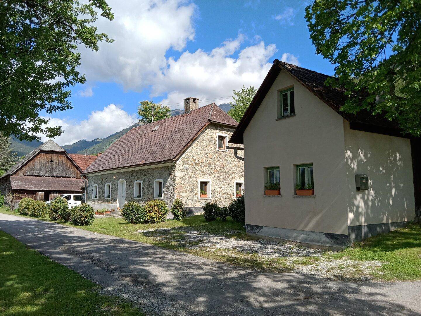 Ensemble aus traditionellem Steinhaus und kleinerem Nebengebäude, eingebettet in eine grüne Landschaft.