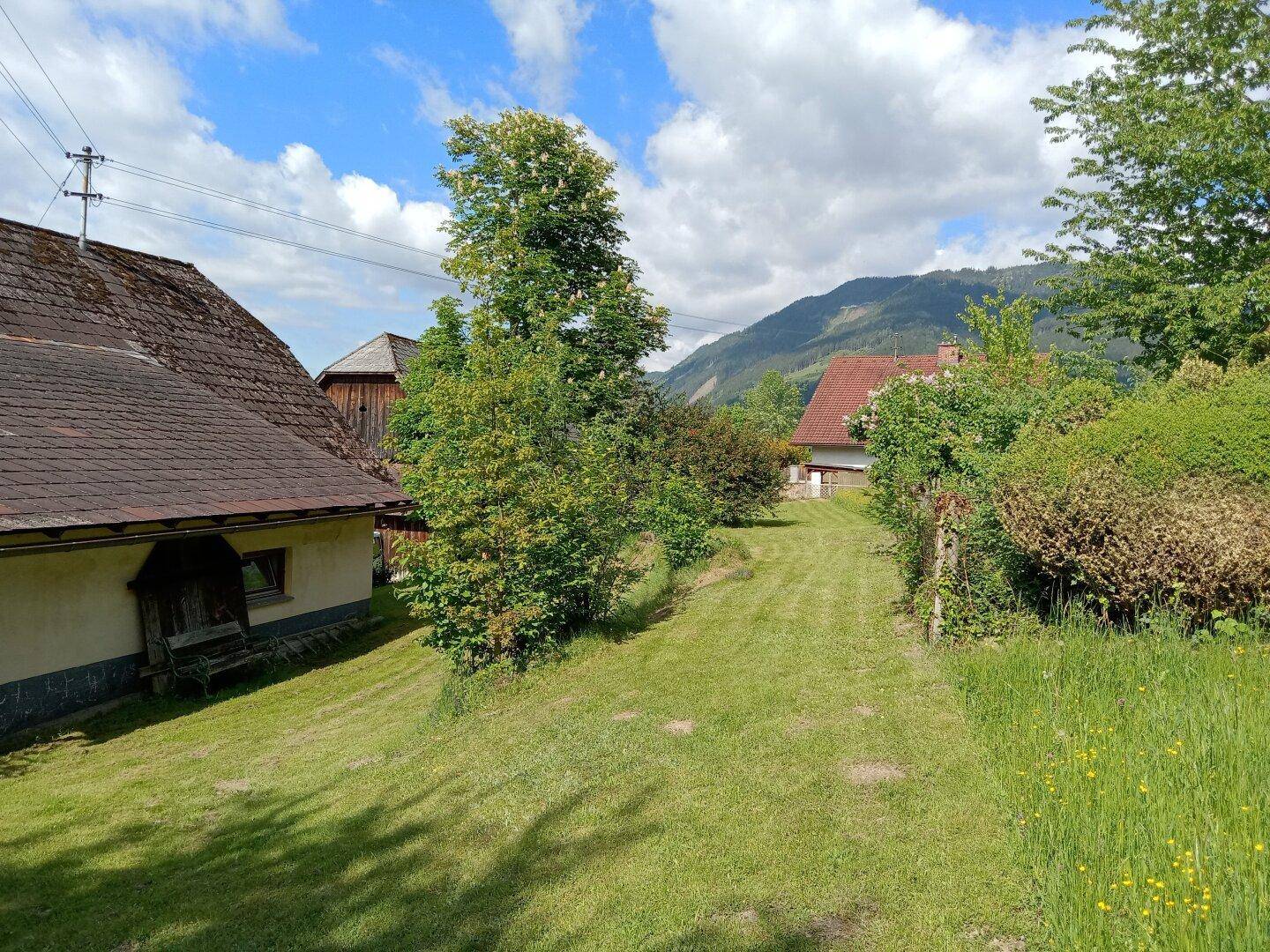 Weitläufige Rasenfläche mit Bäumen und Blick auf die umliegende Hügellandschaft und weitere Gebäude.