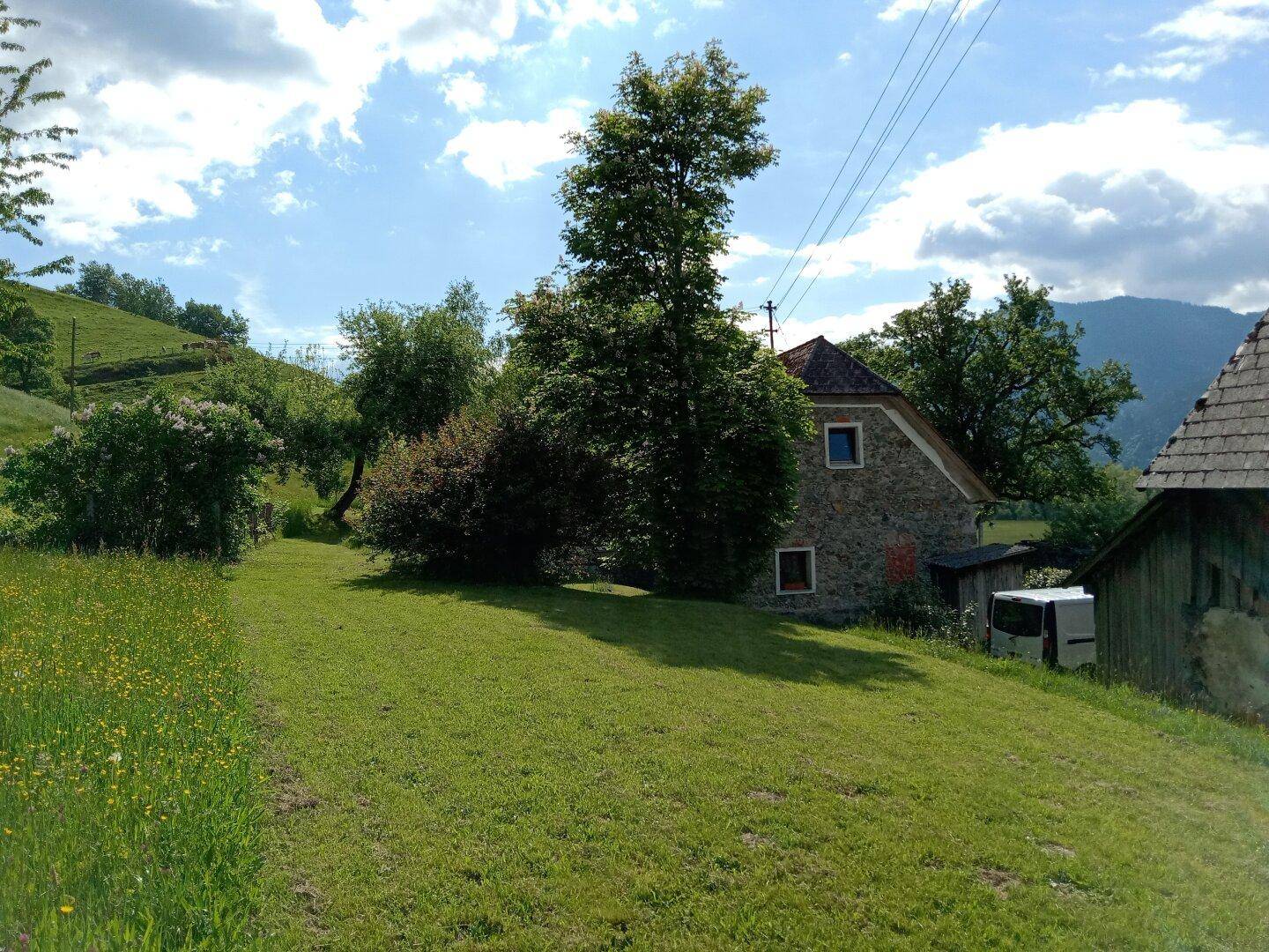 Traditionelles Steinhaus eingebettet in eine grüne Hügellandschaft unter einem bewölkten Himmel.