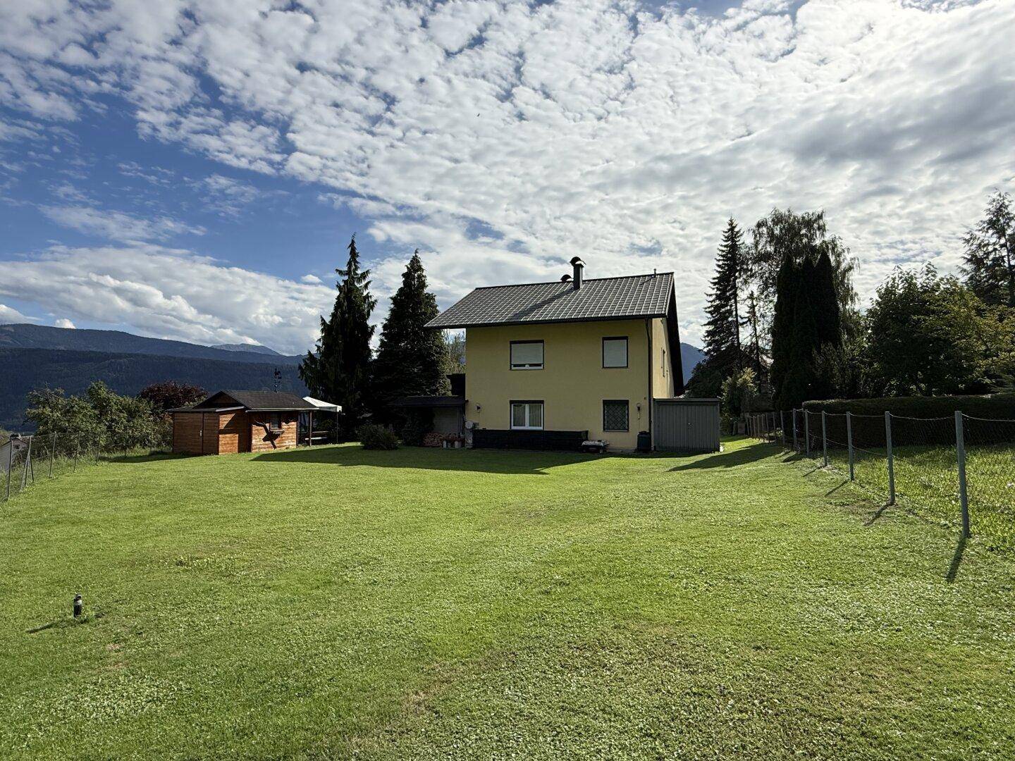 Weitläufiger Gartenbereich hinter dem Haus mit Rasenfläche, Schuppen und Panoramablick auf die Berge.