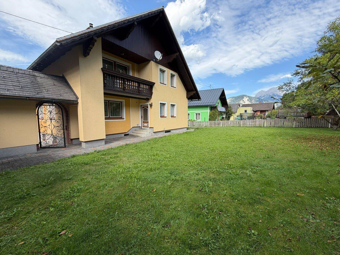 Traditionelles Haus mit großem grünen Rasen und Balkon, umgeben von einer malerischen Berglandschaft.