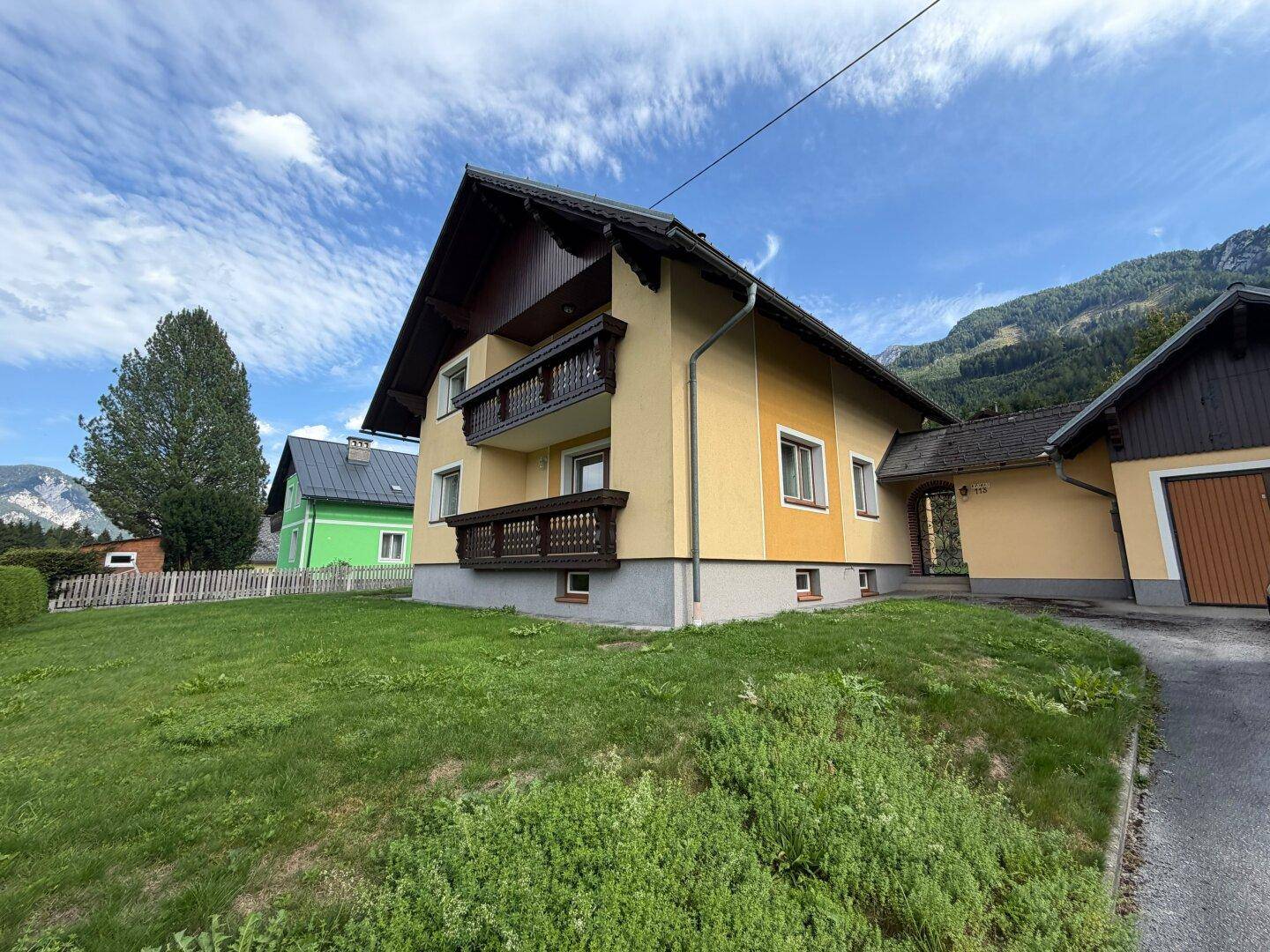 Ansicht des Hauses von der Seite mit Zufahrt, gepflegtem Rasen und der umliegenden Bergkulisse.