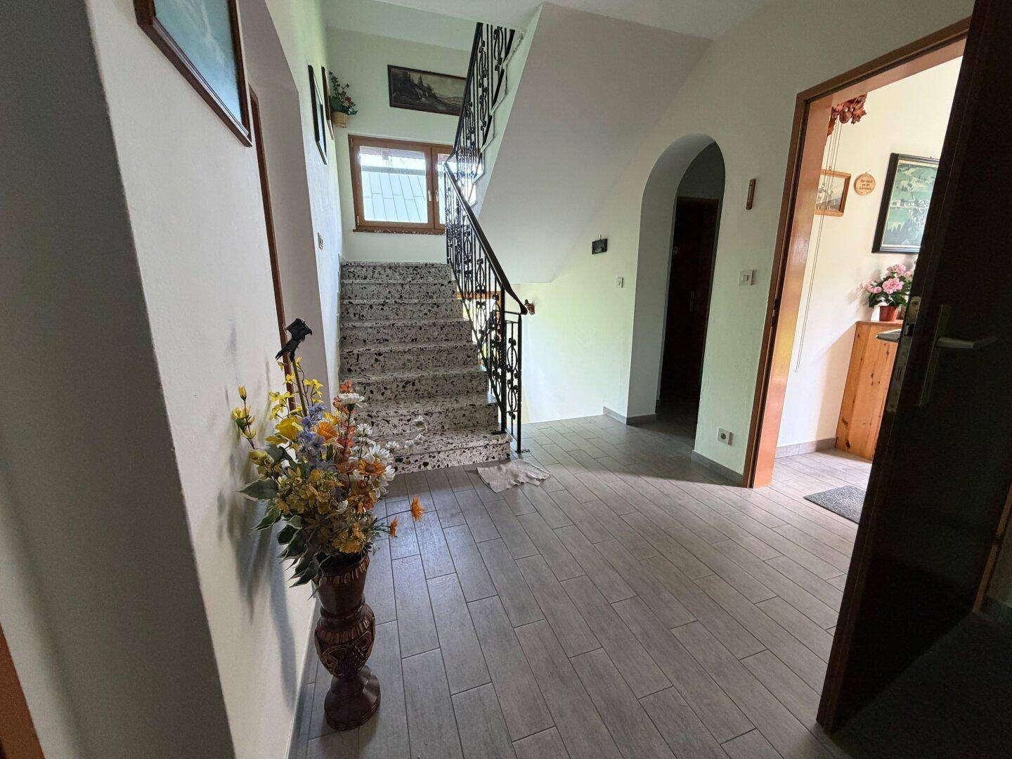 Heller Flur mit Steintreppe, schmiedeeisernem Geländer und modernem Fliesenboden.
