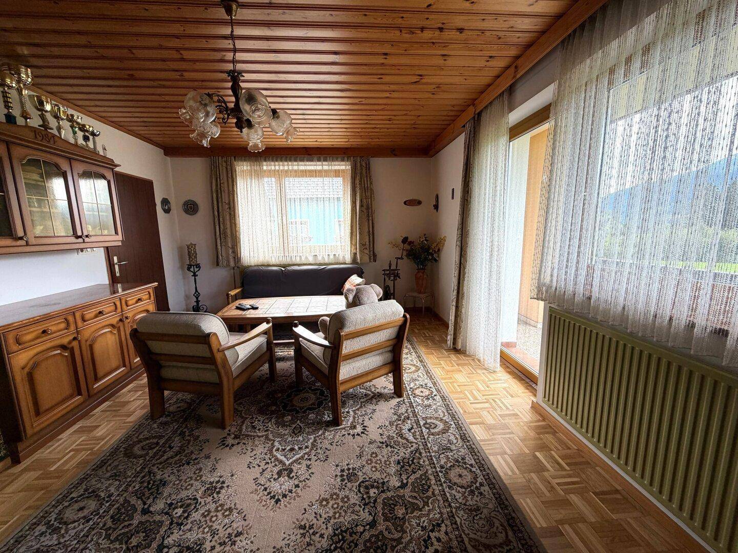Gemütliches Wohnzimmer mit traditionellen Holzmöbeln, Holzdecke und Zugang zu einem Balkon mit Bergblick.