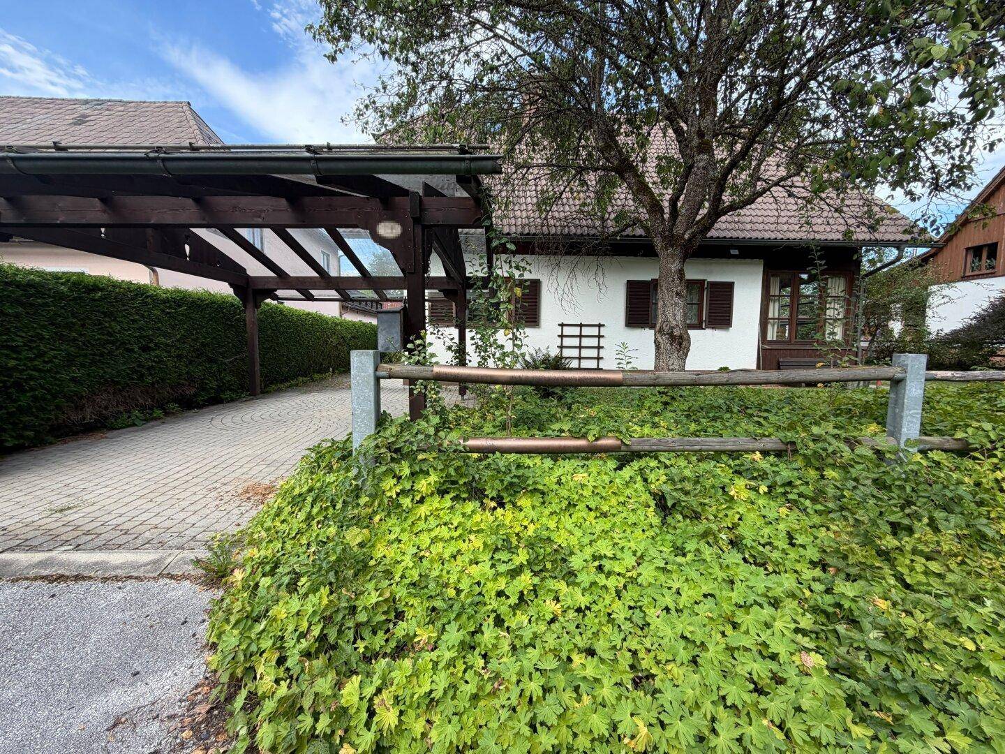 Einfahrt zum Carport und dem charmanten Haus, umgeben von gepflegten Hecken und Bäumen.