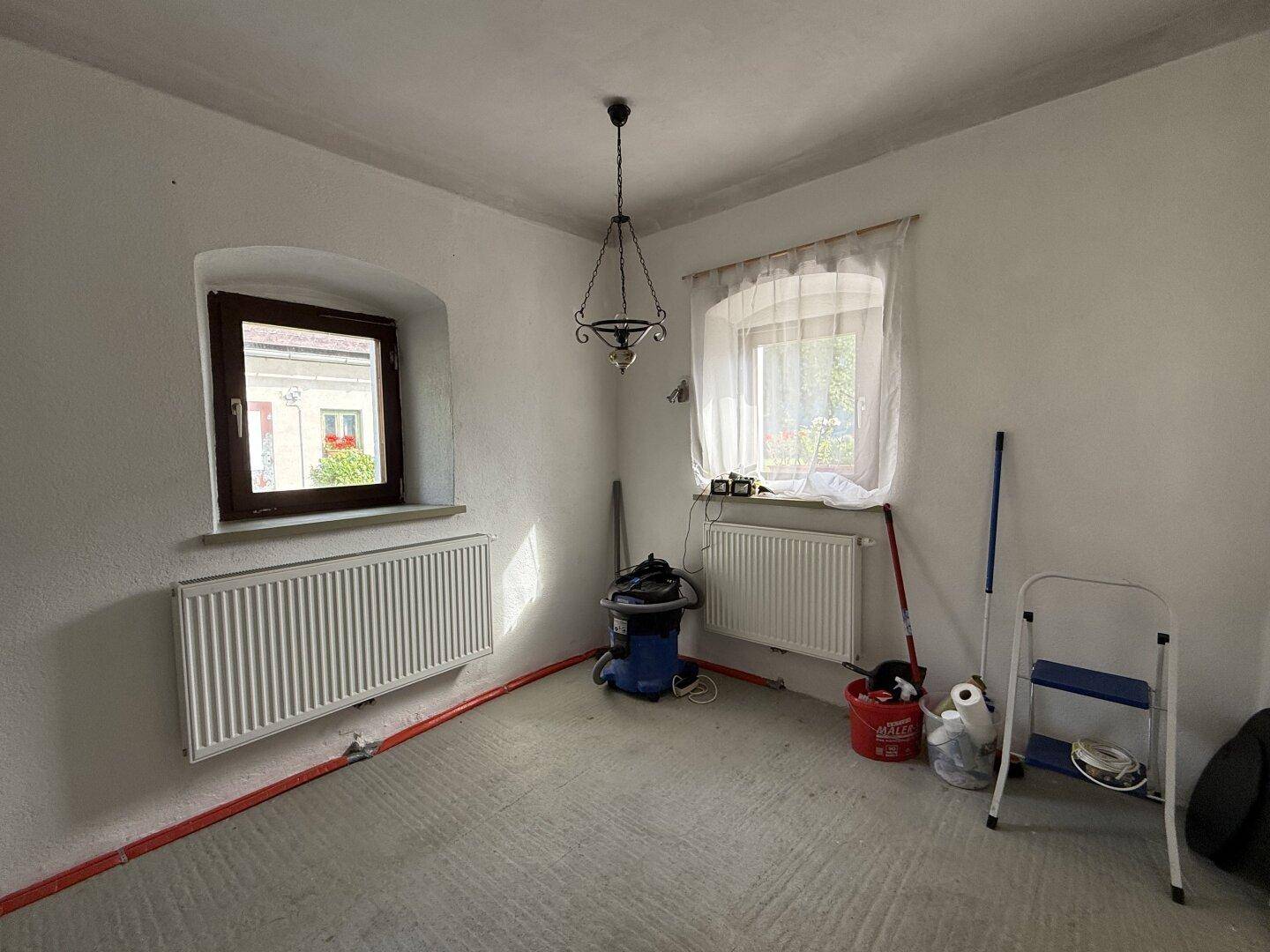 Helles Zimmer mit zwei Fenstern und Heizkörpern, bereit für die weitere Renovierung und Gestaltung.