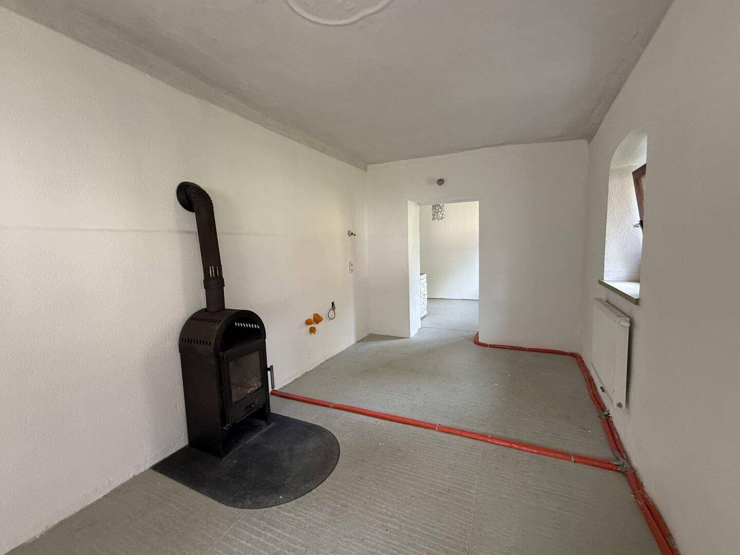 Raum in Renovierung mit einem Holzofen und sichtbaren Installationen, bereit für den Ausbau.