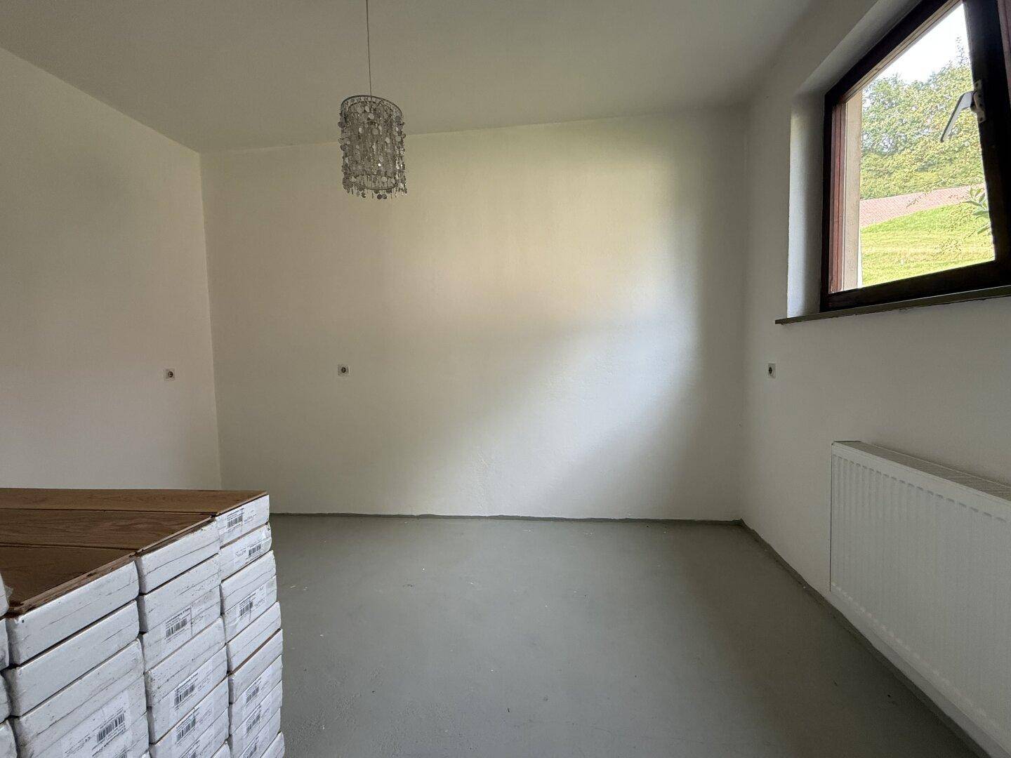Renovierungsbedürftiges Zimmer mit einem Fenster und gestapelten Bodenbelägen, bereit für die Fertigstellung.