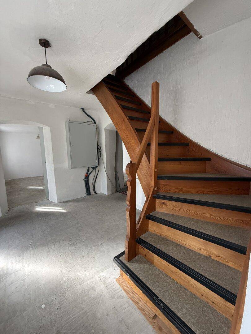 Holztreppe in einem renovierungsbedürftigen Zustand, mit sichtbaren Installationen an der Wand.