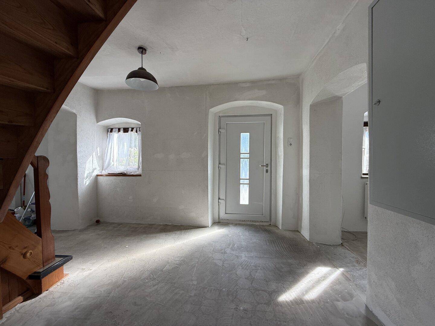 Eingangsbereich mit Holztreppe, weißer Eingangstür und einem kleinen Fenster für Tageslicht.