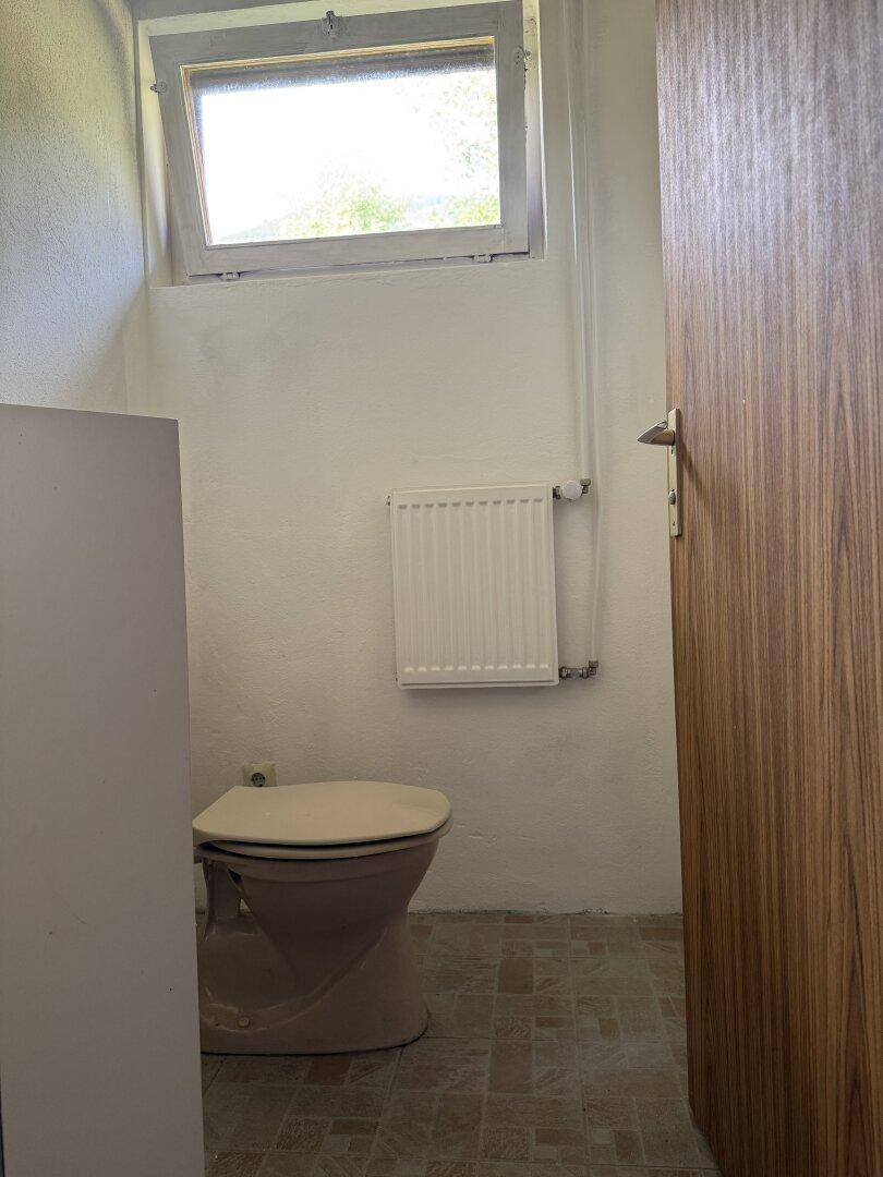 Separate Toilette mit Fenster, Heizkörper und einfacher Ausstattung in hellem Design.