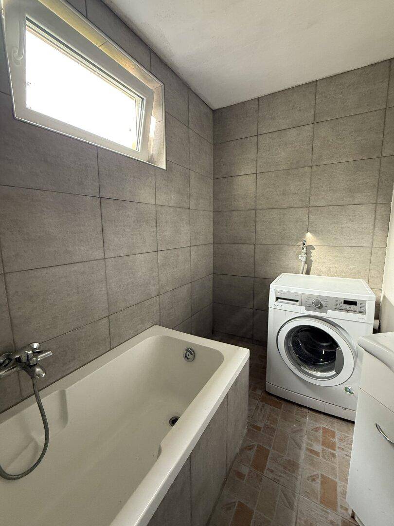 Badezimmer mit Badewanne, Waschmaschine und einem Fenster für natürliches Licht.