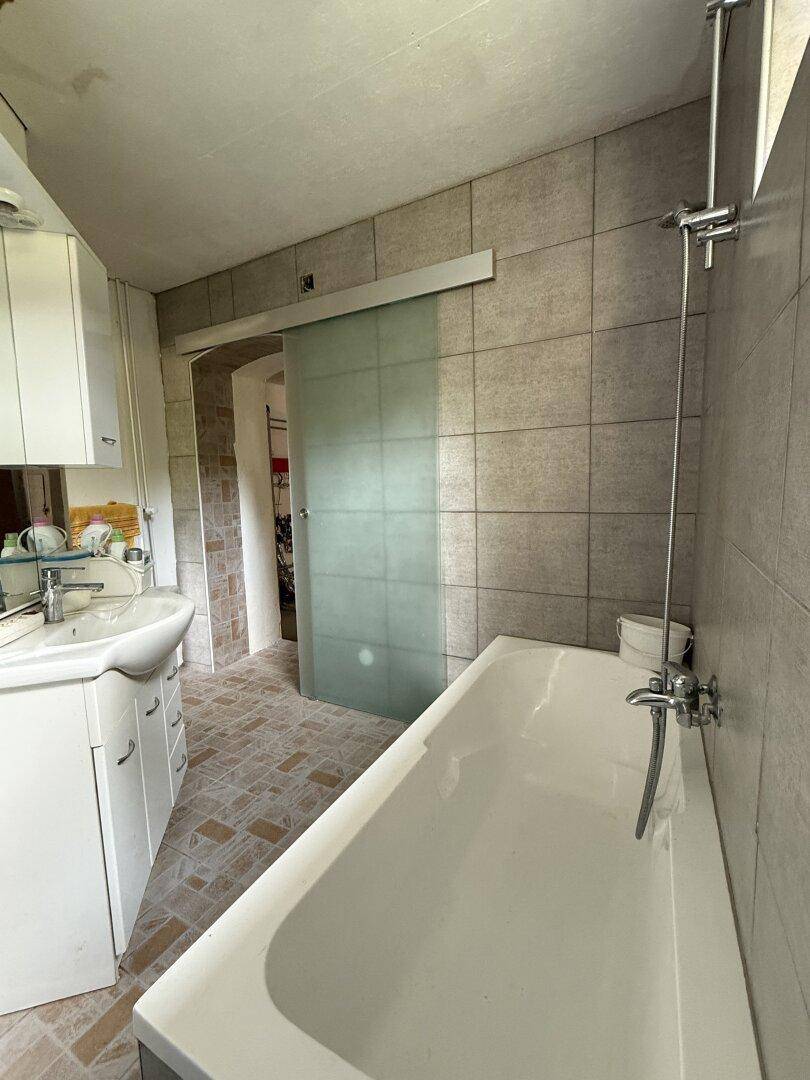 Badezimmer mit Badewanne, Waschbecken und einer Glasschiebetür zum angrenzenden Raum.