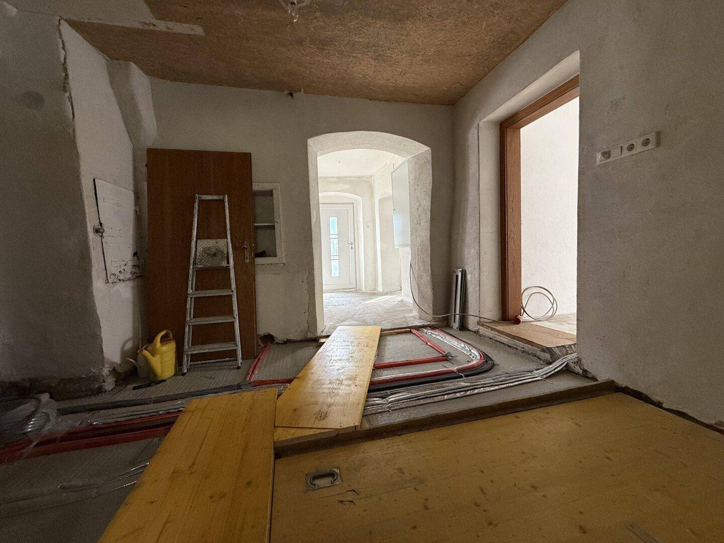 Raum in Renovierung mit sichtbaren Rohren für Fußbodenheizung und Holzdielen.