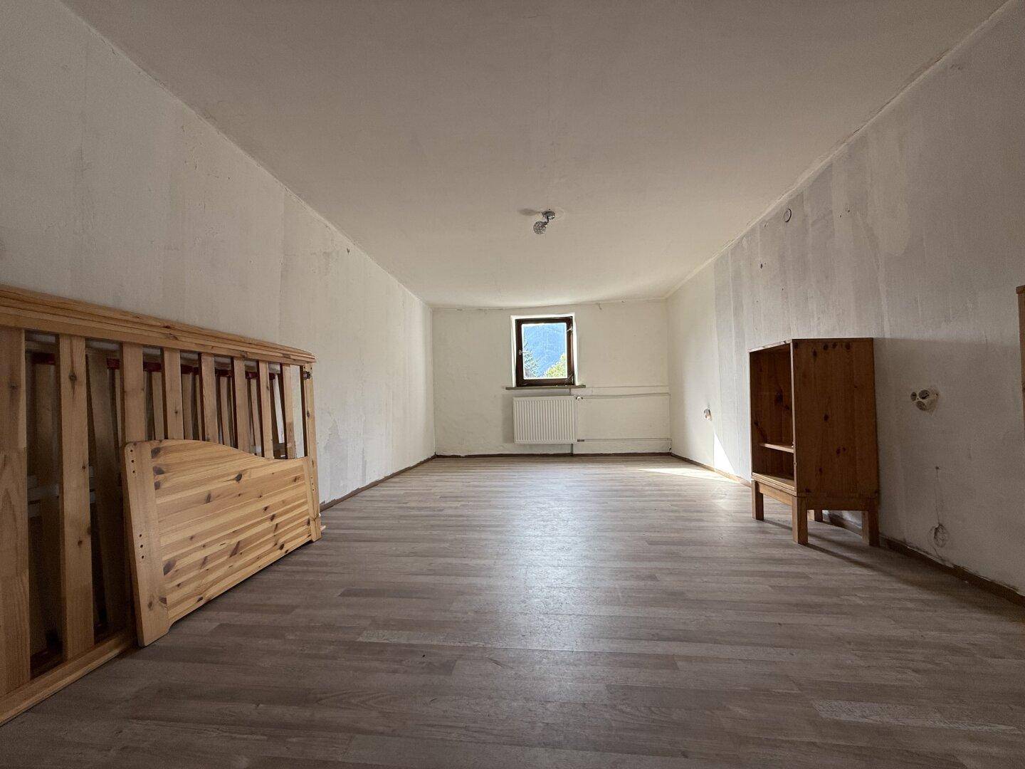 Schlafzimmer mit Laminatboden, einem Fenster und einem zerlegten Bettrahmen aus Holz.