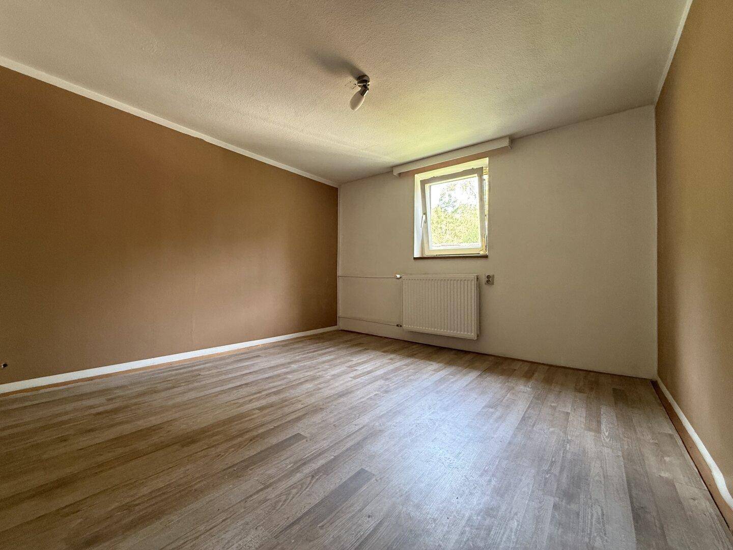Helles Schlafzimmer mit braunen Wänden, Laminatboden und einem Fenster.