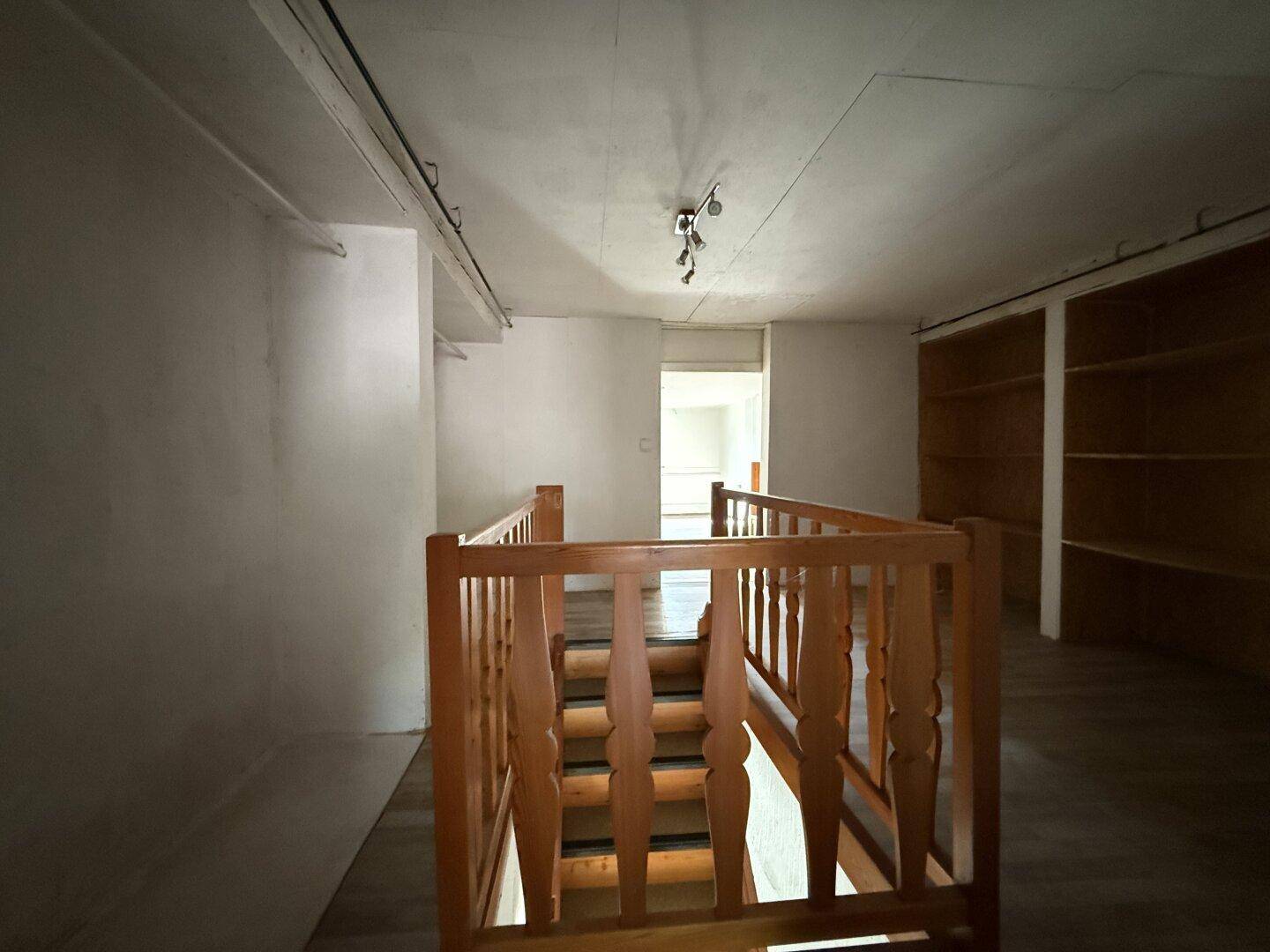 Obergeschoss mit Holztreppe und Blick auf einen weiteren Raum, hell und offen gestaltet.