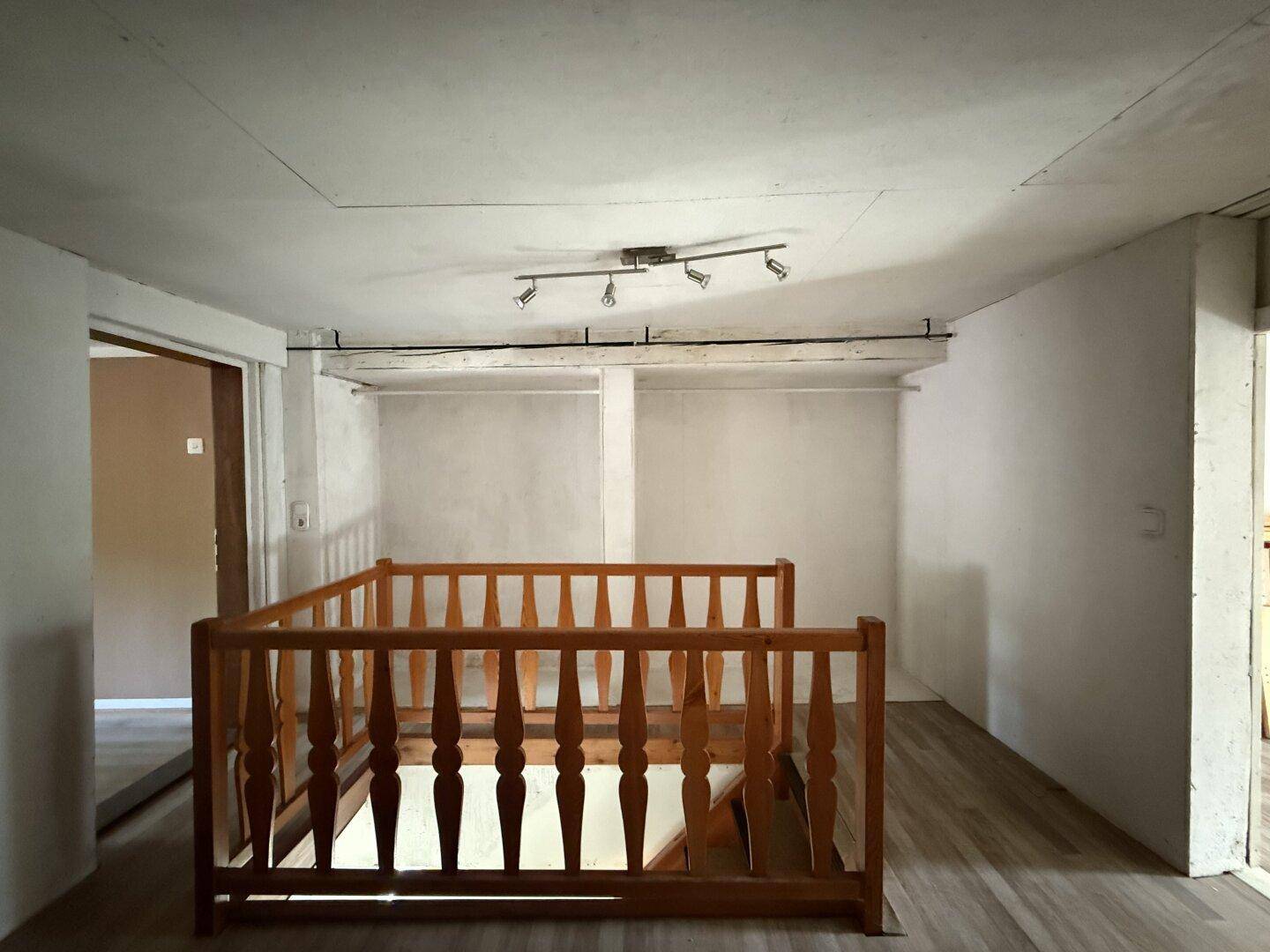 Obergeschoss mit Holztreppe und einem Deckenstrahler, der den Raum beleuchtet.