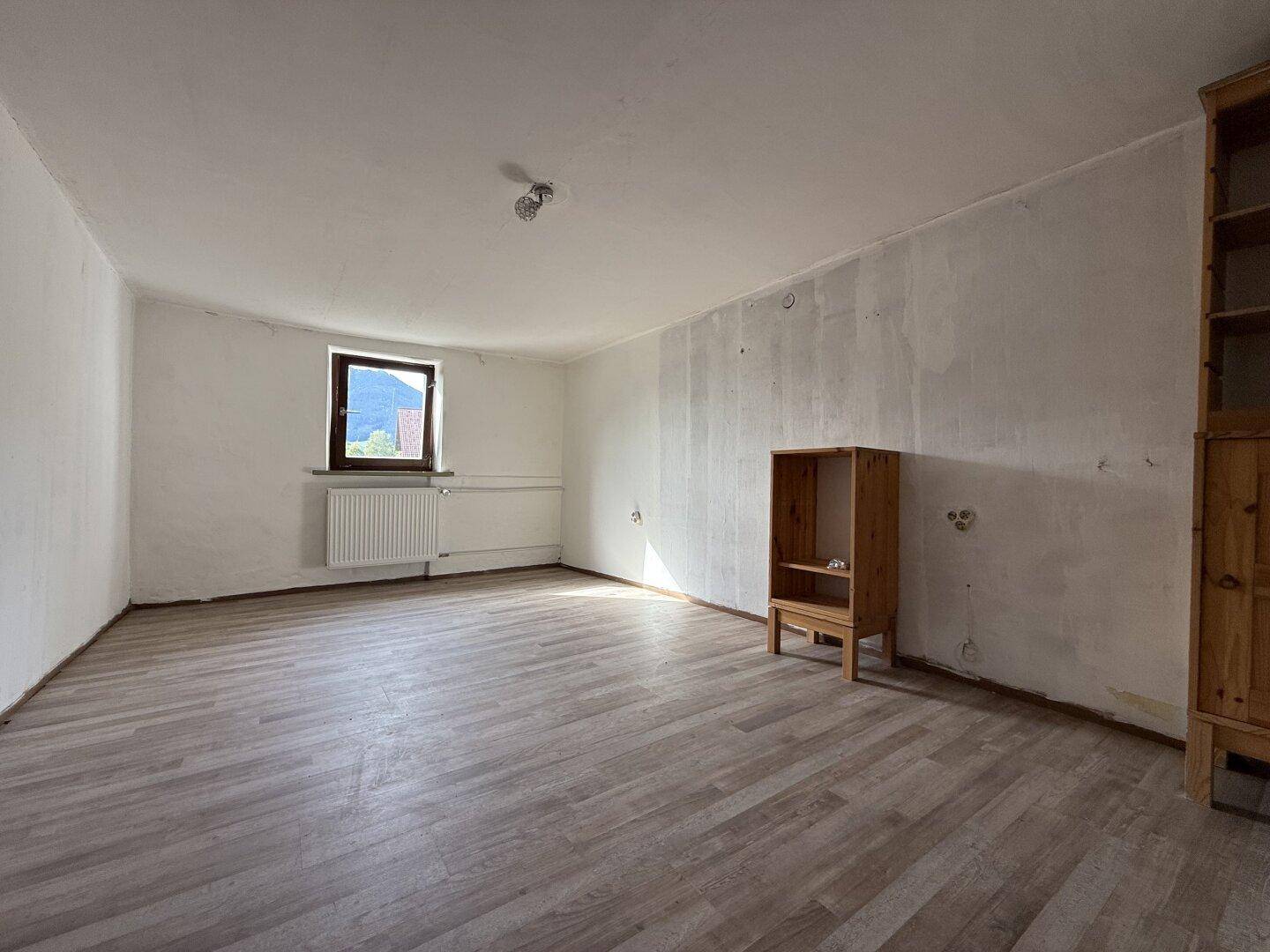 Geräumiges Schlafzimmer mit Laminatboden, einem Fenster und Holzmöbeln.